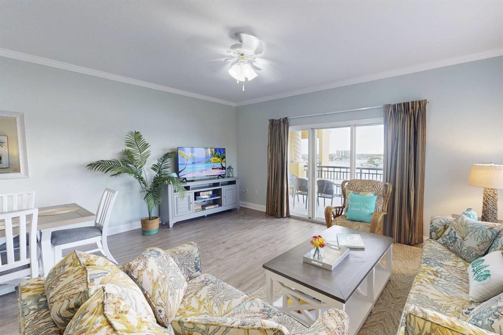 A living room with light blue walls, wood-look flooring, a ceiling fan, and balcony access — 10315 GULF BOULEVARD UNIT 409, TREASURE ISLAND, FL