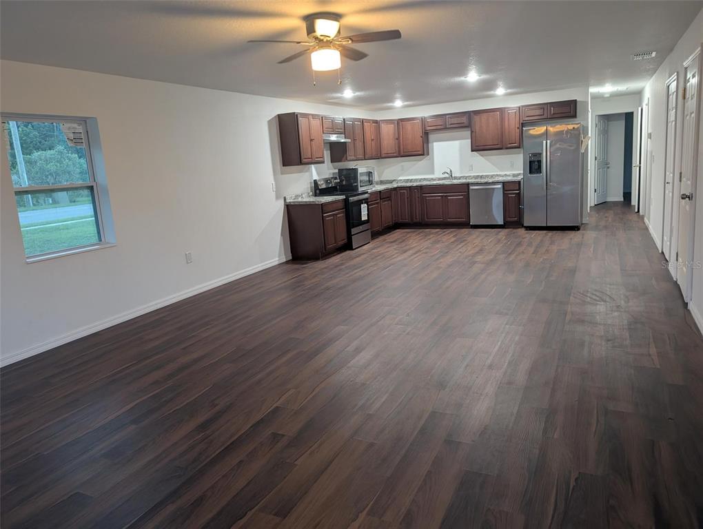 An open-concept kitchen with dark wood cabinets, stainless steel appliances, and dark laminate flooring — 776 E BROADWAY STREET, OVIEDO, FL