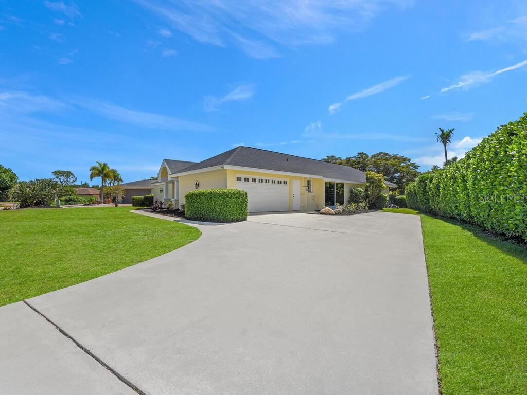A yellow single-story house with a white garage and a large concrete driveway — 491 CYPRESS WAY E, NAPLES, FL
