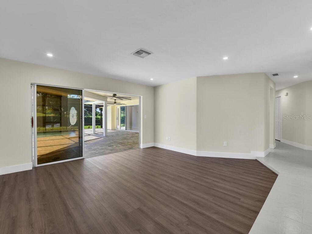 A room with wood-look flooring and a sliding glass door opening to a covered patio — 491 CYPRESS WAY E, NAPLES, FL