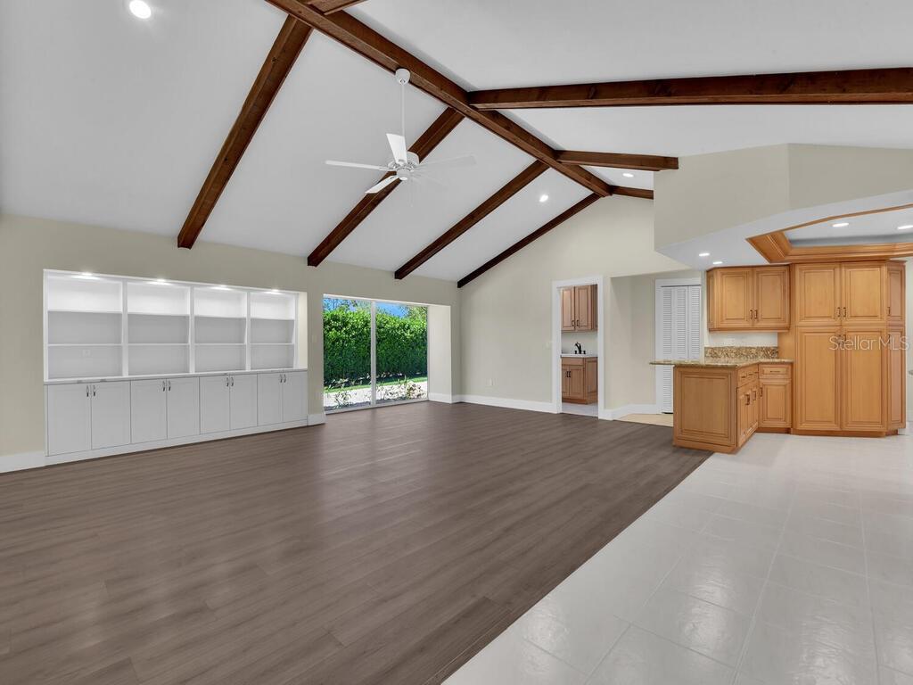 A living room with vaulted wood-beamed ceilings, built-in shelving, and a transition to a kitchen — 491 CYPRESS WAY E, NAPLES, FL