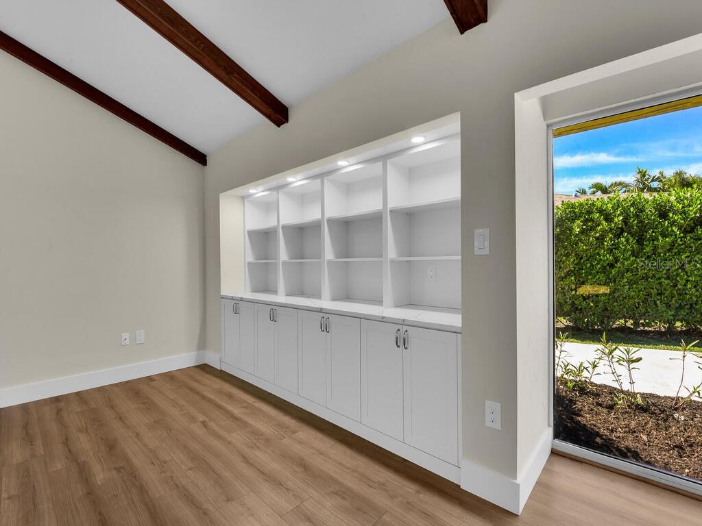 A room with wood-look flooring, a vaulted ceiling with beams, and built-in white shelving units — 491 CYPRESS WAY E, NAPLES, FL