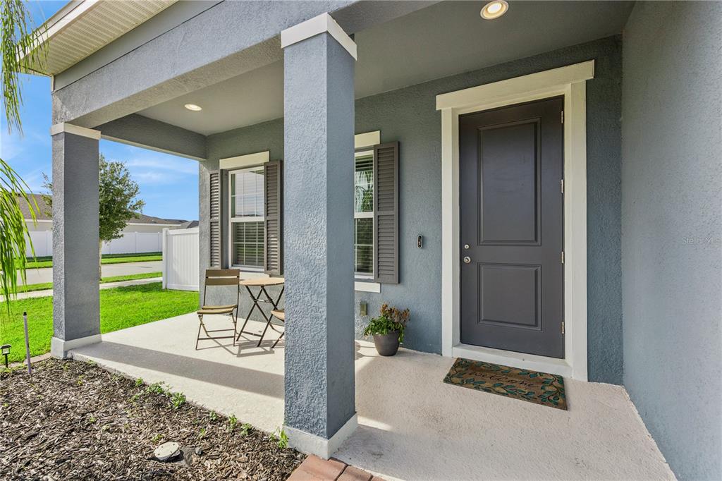 A covered front porch with a dark gray door, concrete floor, and outdoor seating area — 5592 VIGO LOOP, ST CLOUD, FL