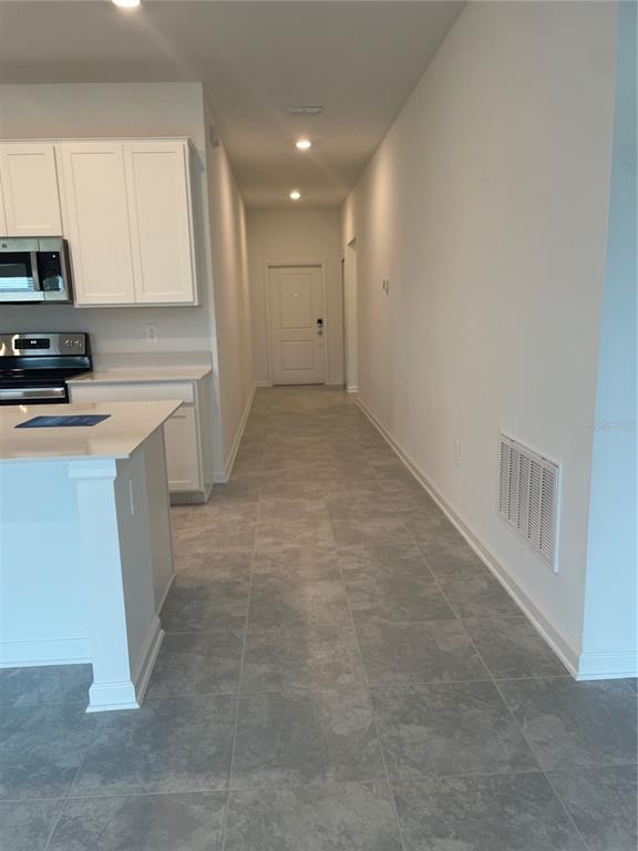 A kitchen with white cabinets and a stone island leads to a hallway with tile — 612 DARING DRIVE, DAVENPORT, FL