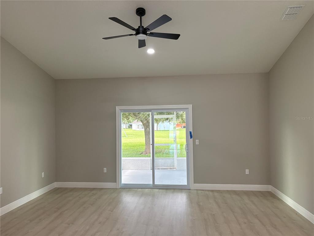 An empty room with light wood-look flooring, a black ceiling fan, and sliding glass doors — 1415 CRISTO REY PLACE, PLANT CITY, FL