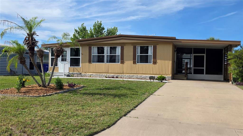 A tan mobile home with a concrete driveway and a screened-in porch under a carport — 1203 APACHE CIRCLE, TAVARES, FL