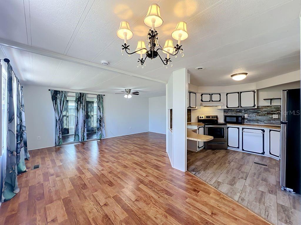 An open-concept living area with wood-look flooring leads into a kitchen with white cabinetry — 1203 APACHE CIRCLE, TAVARES, FL