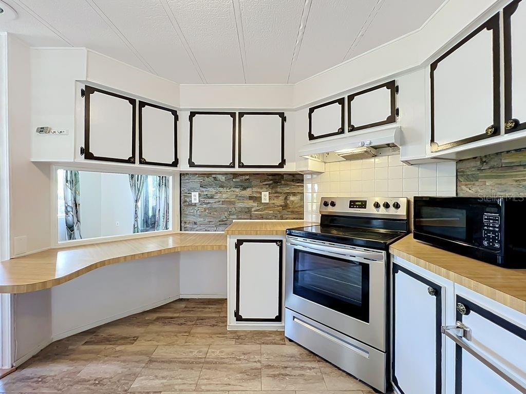 A kitchen features white cabinets with black trim, wood-look countertops, and a stone-tiled backsplash — 1203 APACHE CIRCLE, TAVARES, FL