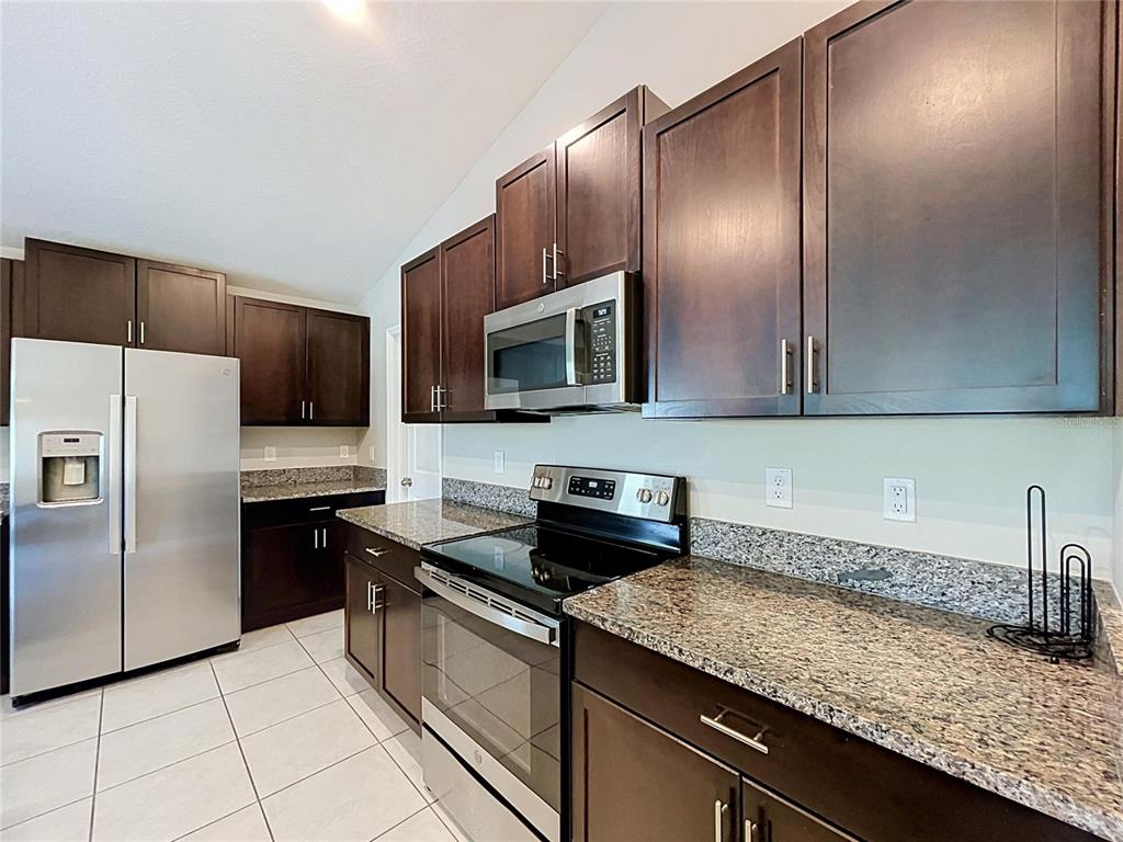 A kitchen features dark wood cabinets, granite countertops, stainless steel appliances, and light tile flooring — 1565 COLDING DRIVE, RUSKIN, FL