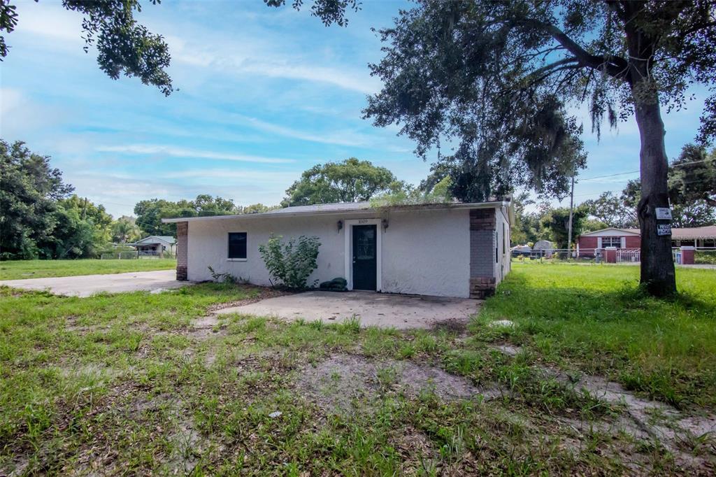 A single-story white house with a concrete patio sits on a grassy lot with trees — 1009 MERCER LOOP, PLANT CITY, FL