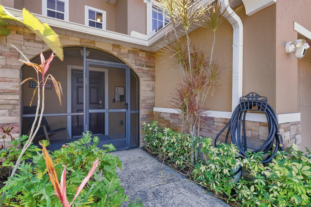 A stone-accented entryway features a screened porch, a walkway, and lush landscaping — 15150 PIPING PLOVER COURT UNIT 103, NORTH FORT MYERS, FL