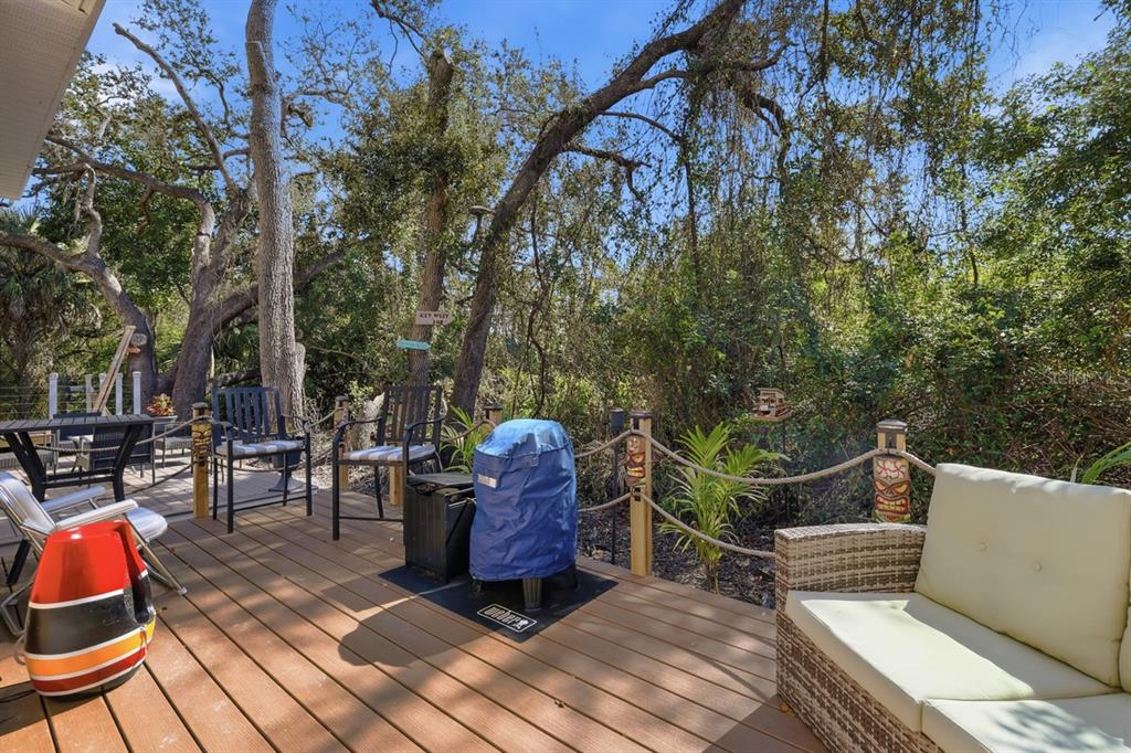 A wooden deck features outdoor furniture, a covered grill, and tiki-themed posts overlooking trees — 15150 PIPING PLOVER COURT UNIT 103, NORTH FORT MYERS, FL