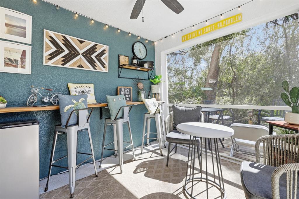 A screened-in porch features a bar counter with stools, teal walls, and outdoor seating — 15150 PIPING PLOVER COURT UNIT 103, NORTH FORT MYERS, FL