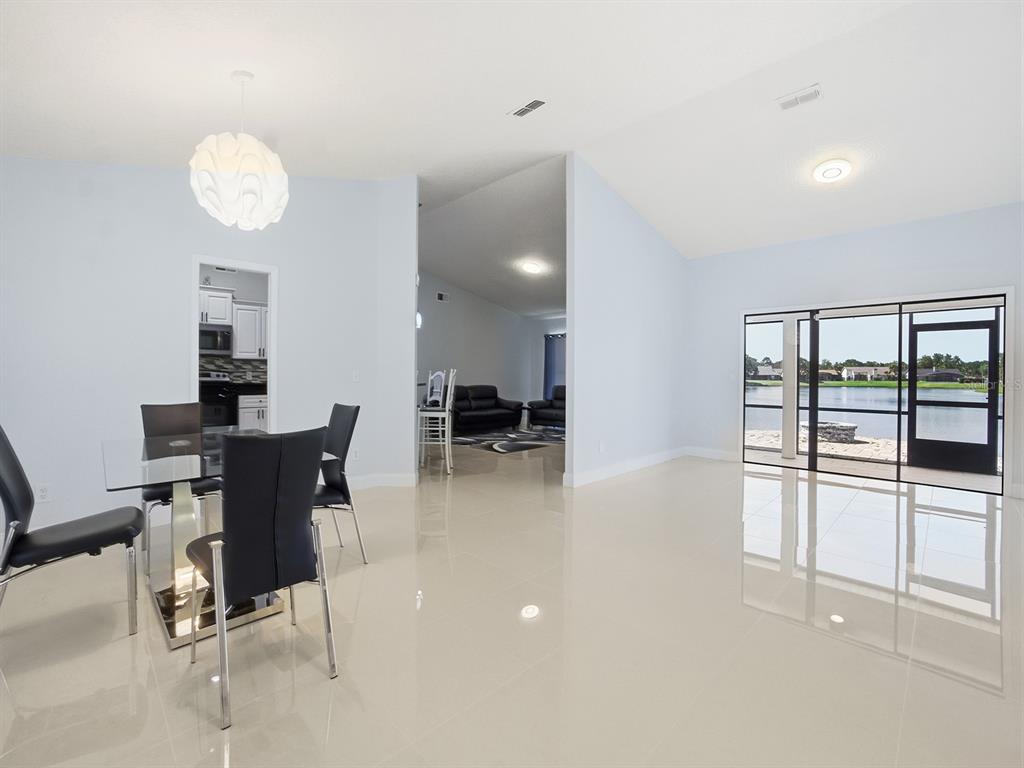A dining area with a glass table and tile floors overlooks a lake through sliding doors — 14712 EAGLES CROSSING DRIVE, ORLANDO, FL