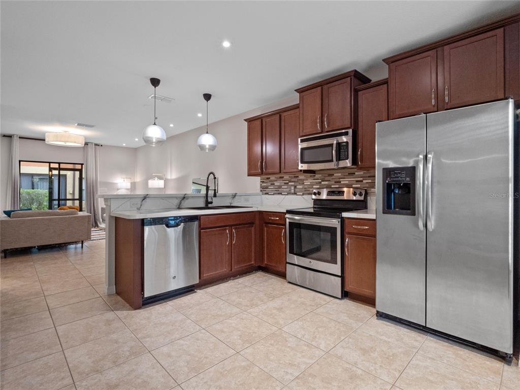A kitchen with wood cabinets, stainless steel appliances, and tile flooring opens to a living area — 2240 TRILLIUM PARK LANE, SANFORD, FL
