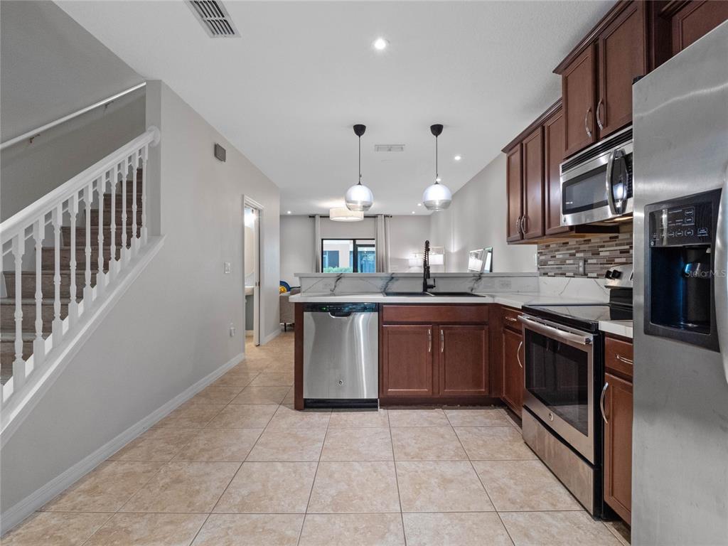 A kitchen with wood cabinets, stainless steel appliances, and tile flooring next to a staircase — 2240 TRILLIUM PARK LANE, SANFORD, FL