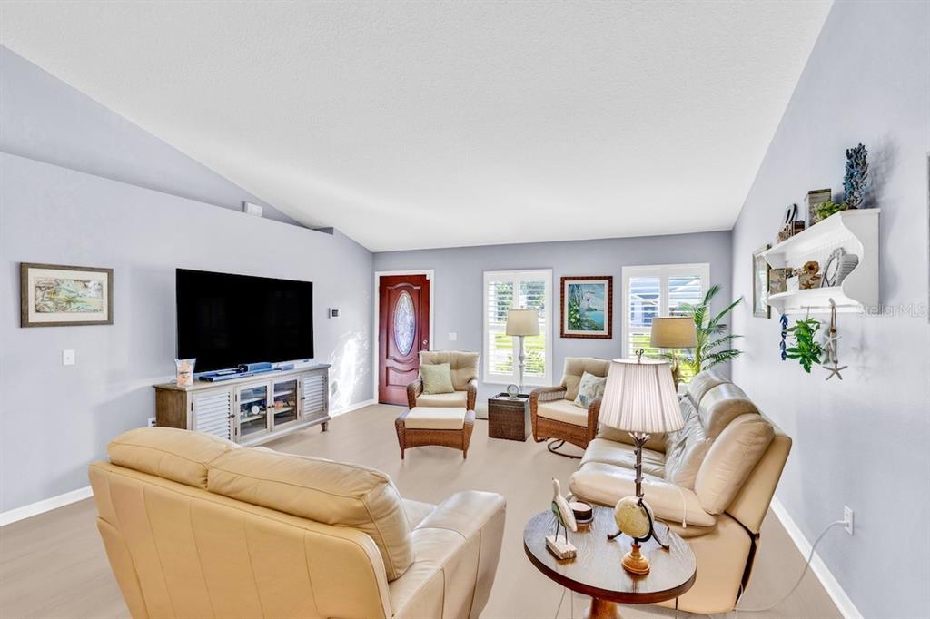 A living room features light-colored flooring, vaulted ceilings, a television console, and beige leather furniture — 1385 HAVERFORD LANE, SEBASTIAN, FL