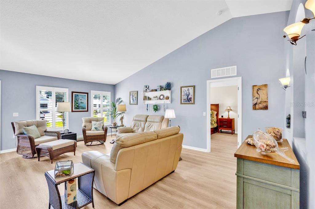 A living room features light blue walls, vaulted ceilings, light wood flooring, and beige furniture — 1385 HAVERFORD LANE, SEBASTIAN, FL
