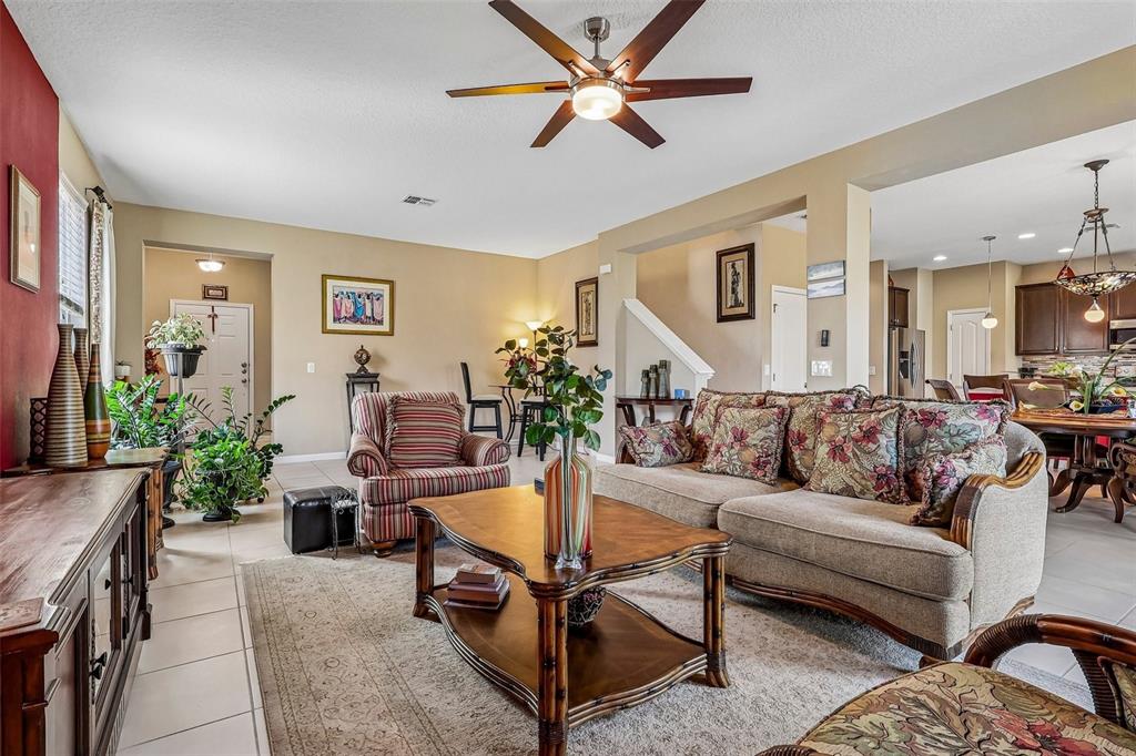A living room features a beige sofa, striped armchair, wooden coffee table, and ceiling fan — 16700 ABBEY HILL COURT, CLERMONT, FL