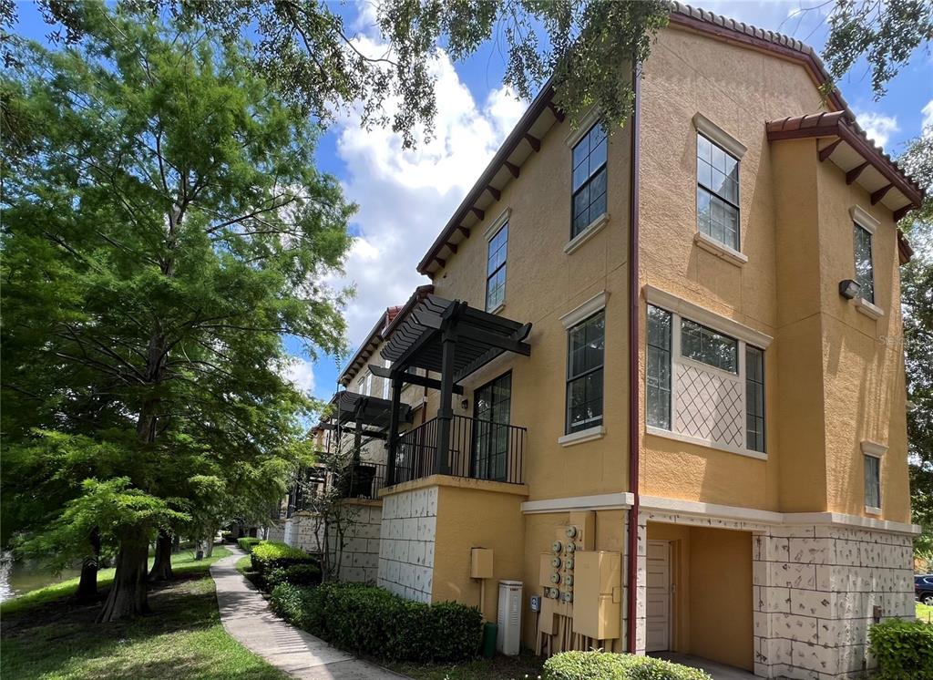 A three-story yellow stucco townhouse with a pergola-covered balcony and a stone-veneer lower level — 6121 METROWEST BOULEVARD UNIT 101, ORLANDO, FL