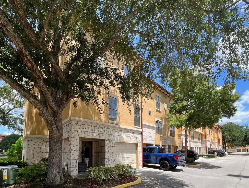 A three-story townhouse exterior with a tan stucco facade, stone accents, and a blue truck — 6121 METROWEST BOULEVARD UNIT 101, ORLANDO, FL