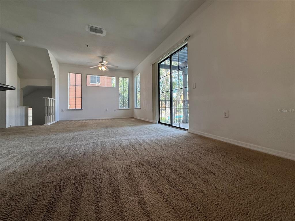 An empty living room features beige carpeting, a ceiling fan, and a sliding glass door — 6121 METROWEST BOULEVARD UNIT 101, ORLANDO, FL