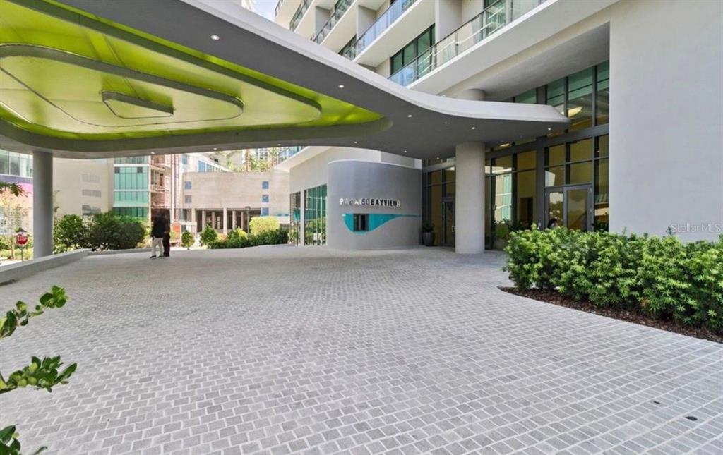 A paved driveway leads to the modern entrance of a multi-story building with a green canopy — 501 NE 31ST STREET UNIT 1808, MIAMI, FL