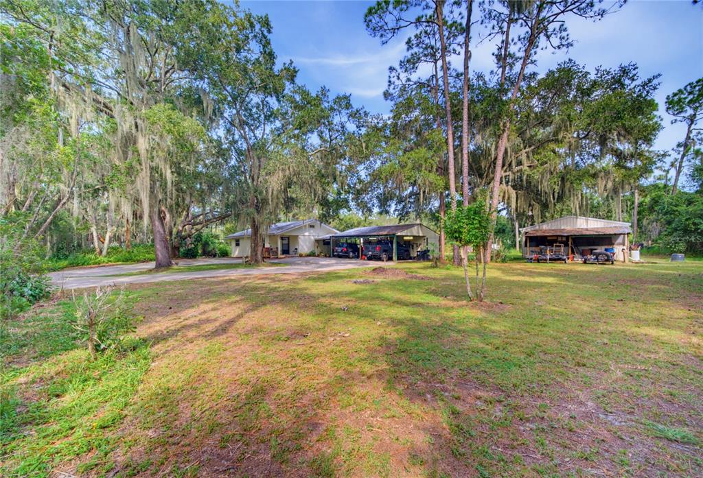 A house with a carport and a detached shed sits on a large, wooded lot — 10930 CAMP MACK ROAD, LAKE WALES, FL