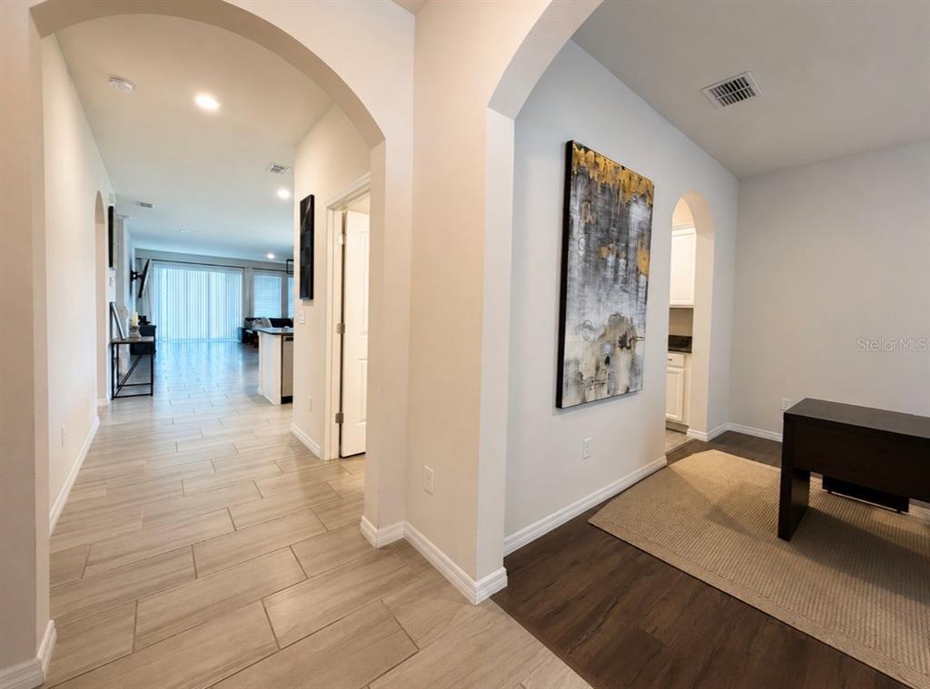 A hallway with light tile flooring leads toward a living area, adjacent to a study — 431 HALTER DRIVE, APOPKA, FL