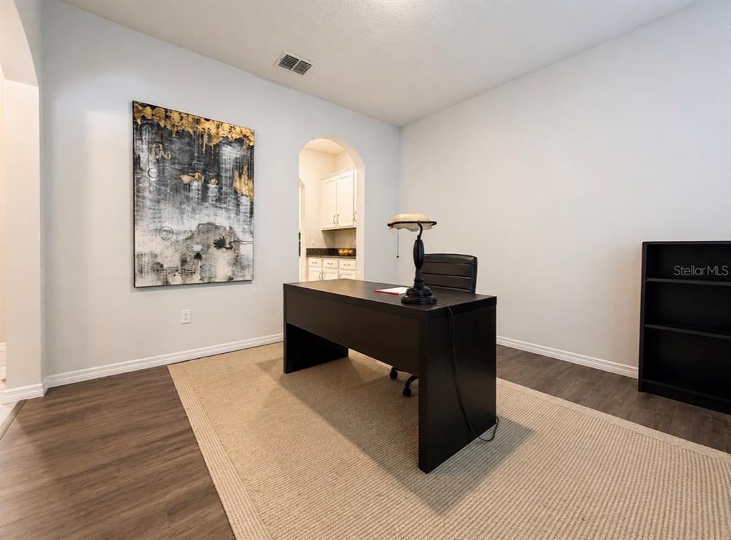 A home office features a dark desk, a rug, wall art, and an arched doorway — 431 HALTER DRIVE, APOPKA, FL