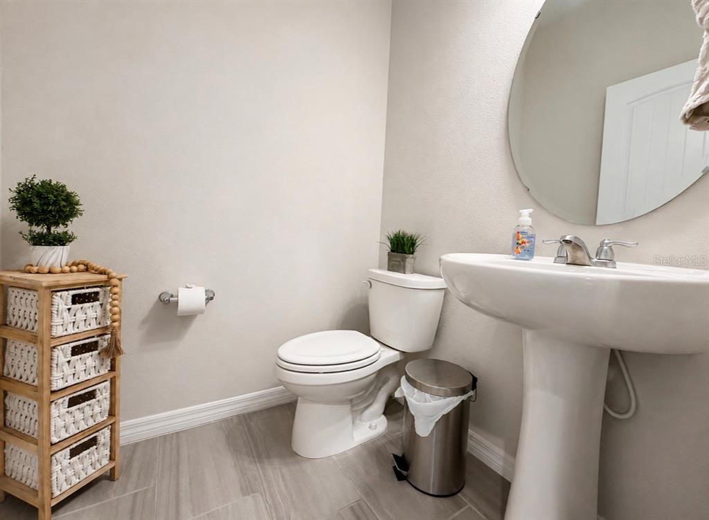 A small bathroom features a pedestal sink, a toilet, a round mirror, and storage shelving — 431 HALTER DRIVE, APOPKA, FL