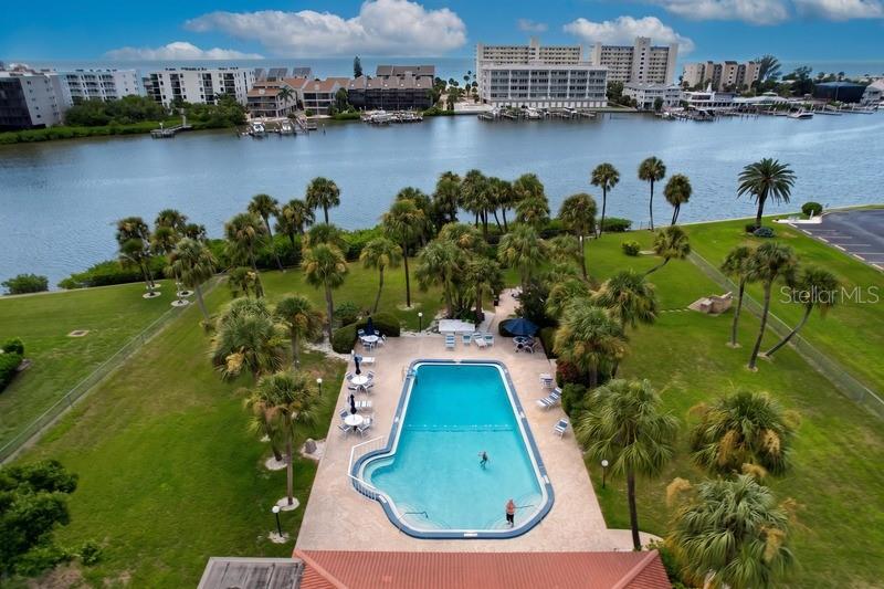 An aerial view shows a swimming pool surrounded by palm trees, grass, and waterfront buildings — 10351 REGAL DRIVE UNIT 5, LARGO, FL