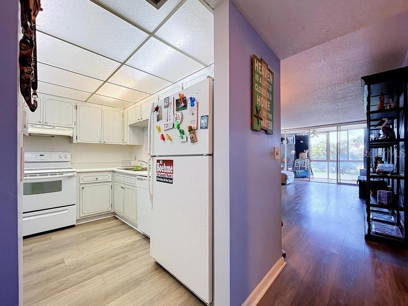 A kitchen with white cabinets and appliances opens into a living area with wood floors — 10351 REGAL DRIVE UNIT 5, LARGO, FL