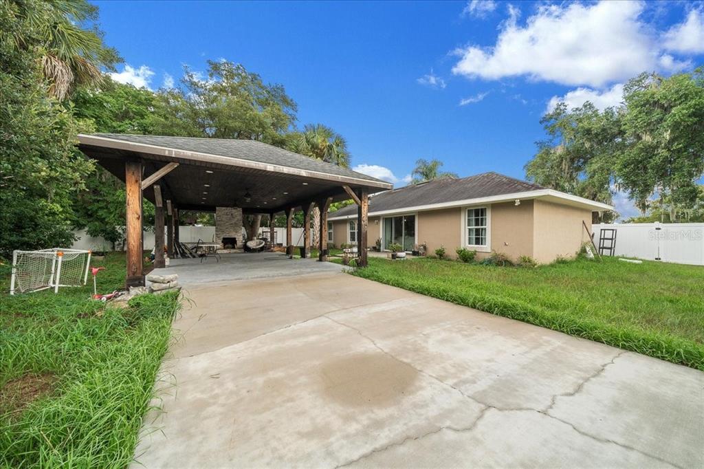 A backyard features a large covered patio with a stone fireplace and a concrete driveway — 60 OWENS STREET, UMATILLA, FL