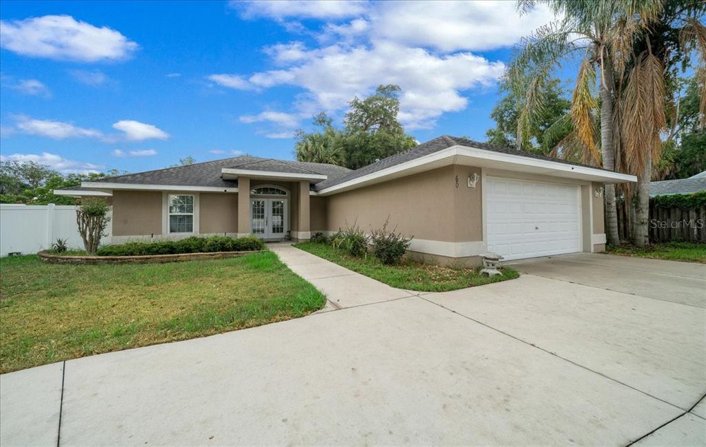 A single-story house with a tan stucco exterior, a two-car garage, and a concrete driveway — 60 OWENS STREET, UMATILLA, FL