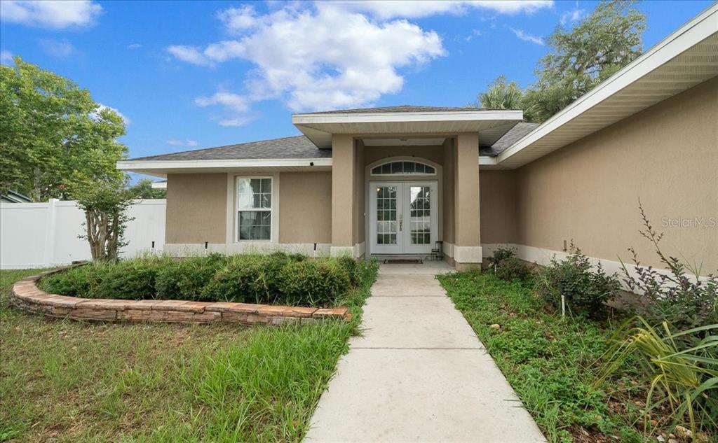 A tan house with a concrete walkway leading to a white double front door — 60 OWENS STREET, UMATILLA, FL
