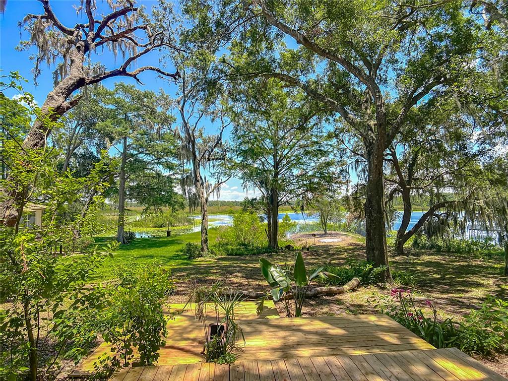 A wooden deck overlooks a grassy yard with mature trees and a lake in the distance — 8781 S LAKESHORE DRIVE, FLORAL CITY, FL