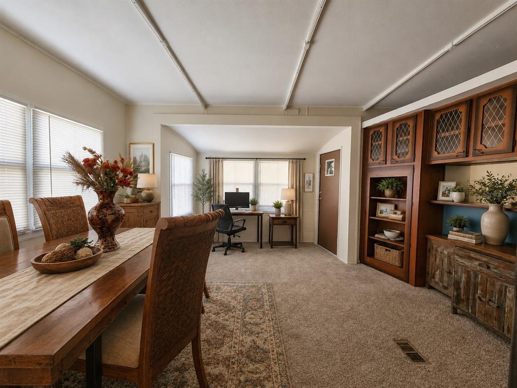 A dining area with a wooden table leads into a carpeted living space with office furniture — 3074 LARKIN ROAD, MIMS, FL