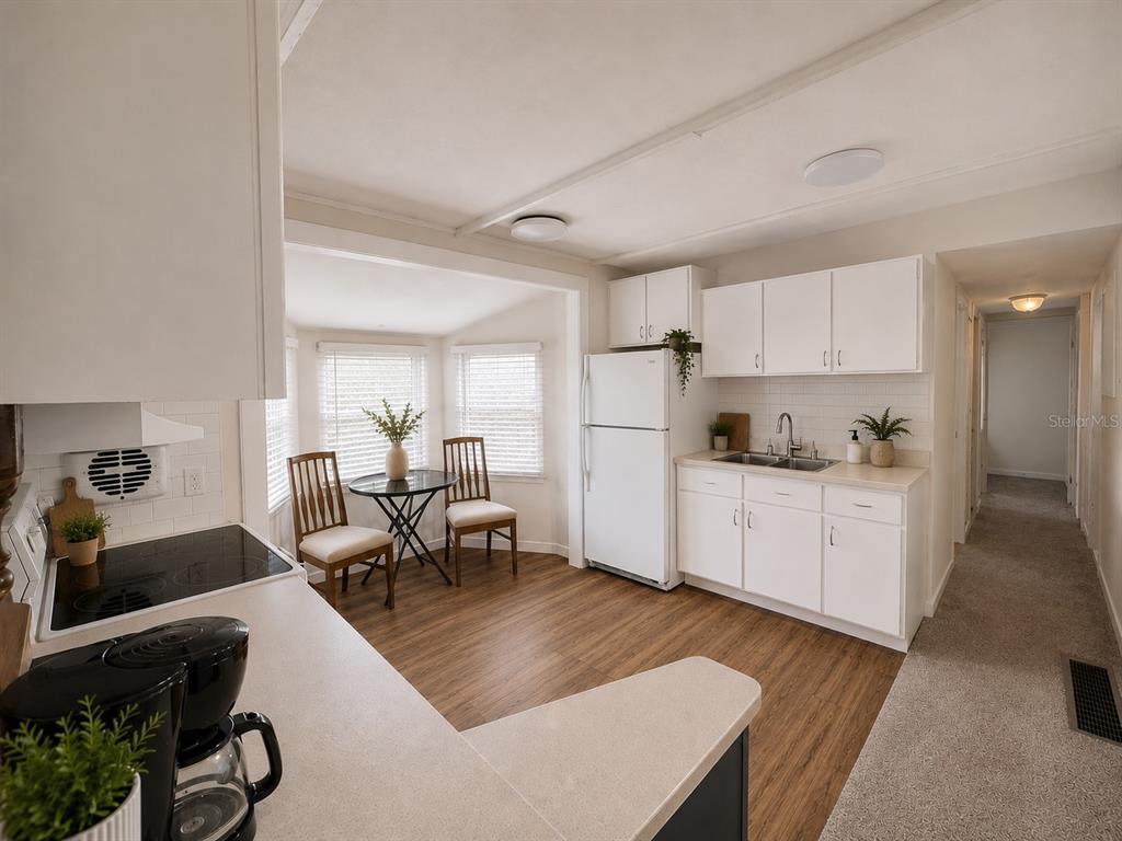 A kitchen with white cabinets, a white refrigerator, and a small dining area with windows — 3074 LARKIN ROAD, MIMS, FL