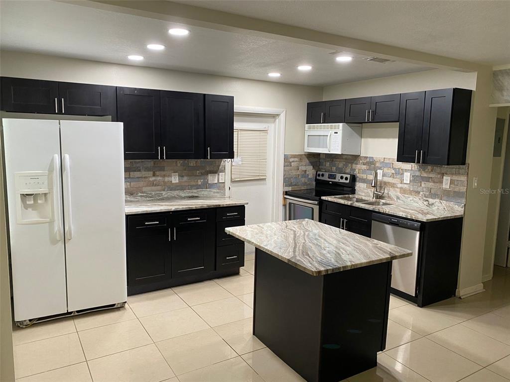 A kitchen features dark cabinets, granite countertops, a center island, and light tile flooring — 2605 PEMBROOK DRIVE, ORLANDO, FL