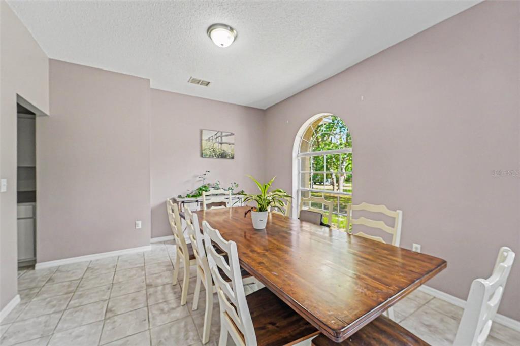A dining room features a wooden table, white chairs, tile flooring, and an arched window — 10724 PATRICK AVE, HUDSON, FL