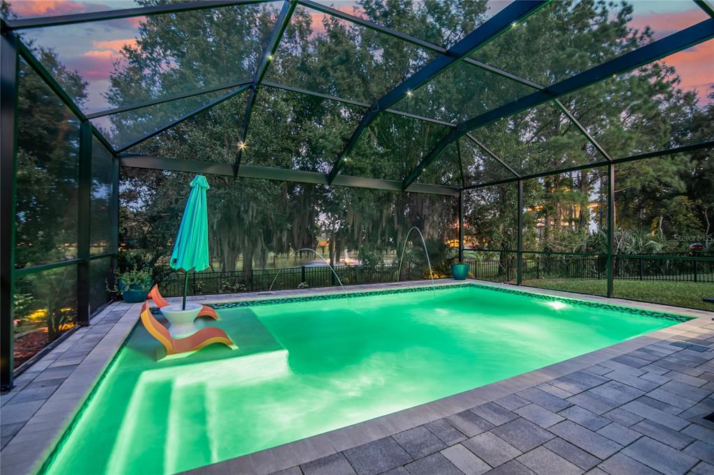 A screened-in swimming pool with a tanning ledge, lounge chairs, and water features at dusk — 4346 O ROURKE COURT, WESLEY CHAPEL, FL