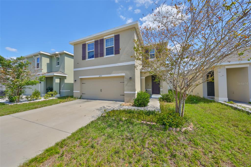 A two-story suburban house with a tan stucco exterior, a two-car garage, and a driveway — 10967 CARLTON FIELDS DRIVE, RIVERVIEW, FL