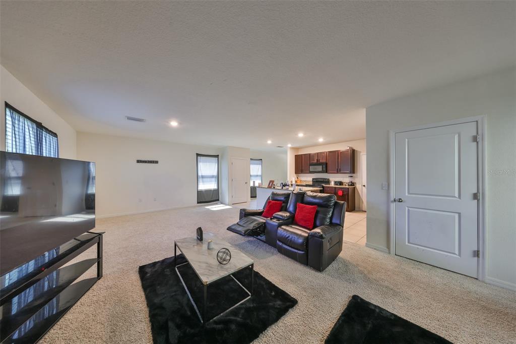 A living room with beige carpet, a black leather recliner, and an open kitchen — 10967 CARLTON FIELDS DRIVE, RIVERVIEW, FL