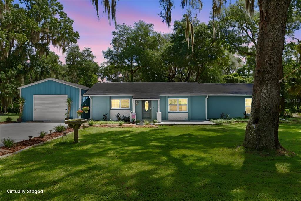 A blue single-story house with a detached garage sits on a grassy lot with trees — 7625 S ANNIE TERRACE, FLORAL CITY, FL