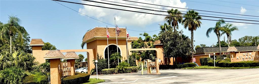 The exterior of the New Atlantis Club features a tan building with arched entryways and flags — 12760 INDIAN ROCKS ROAD UNIT 562, LARGO, FL