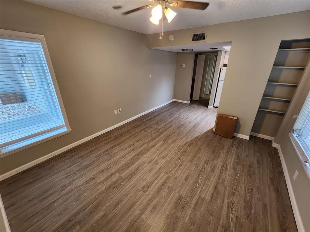 An empty room with wood-look flooring, a ceiling fan, built-in shelving, and a large window — 705 1ST STREET UNIT 3, INDIAN ROCKS BEACH, FL