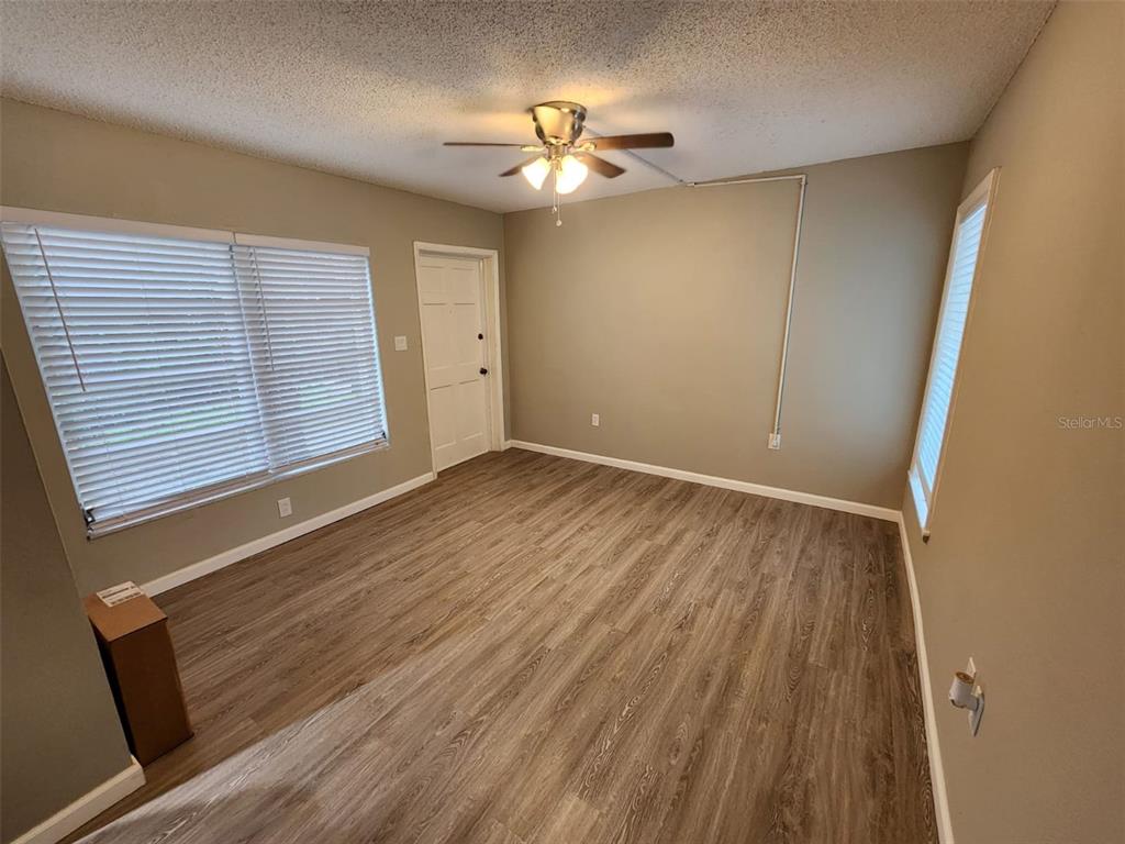 An empty room features wood-look flooring, a ceiling fan, and white blinds on the windows — 705 1ST STREET UNIT 3, INDIAN ROCKS BEACH, FL