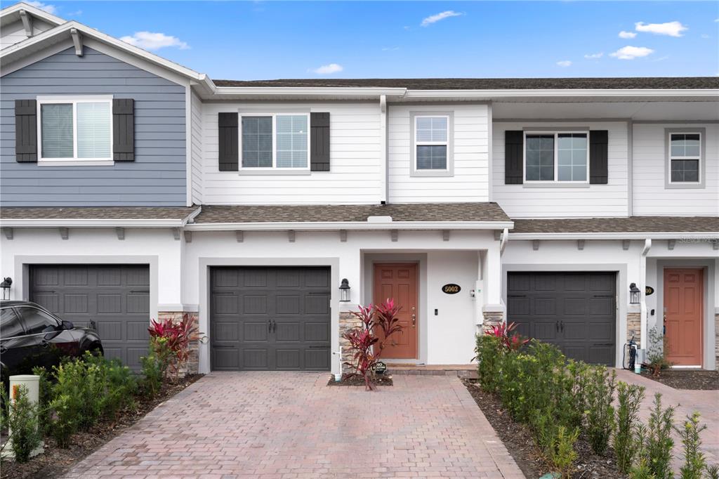 A two-story townhouse exterior features a brick driveway, garage, and a brown front door — 5002 RAIN SHADOW DRIVE, ST CLOUD, FL
