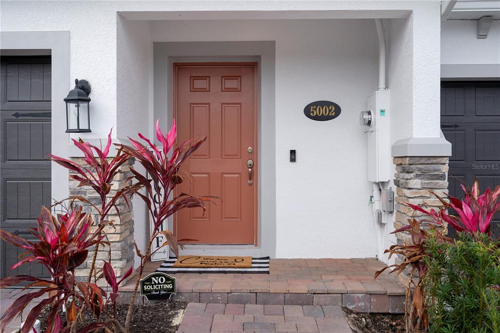 The exterior entrance features a terracotta-colored door, a brick walkway, and two potted plants — 5002 RAIN SHADOW DRIVE, ST CLOUD, FL